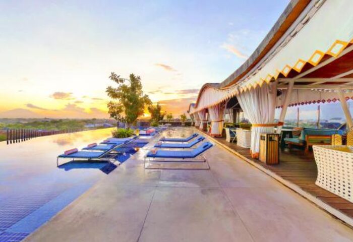 TS Suites Seminyak gay-friendly hotel rooftop infinity pool at sunset. Lounge chairs line the pool's edge, with a covered bar area nearby.