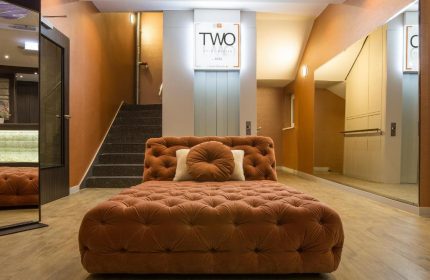 TWO Hotel Berlin by Axel, an adults-only gay-friendly hotel. Lobby seating area with tufted chaise lounge, stairs, and elevator. Modern design.