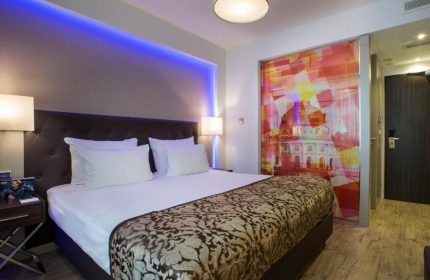 TWO Hotel Berlin by Axel room. Gay-friendly adults-only hotel with modern design, blue lighting, comfortable bed, and artistic decor.