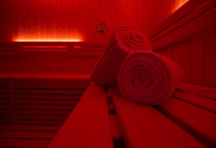 Sauna at TWO Hotel Berlin by Axel, an adults-only, gay-friendly hotel. Rolled towels rest on the wooden benches, illuminated by red light.
