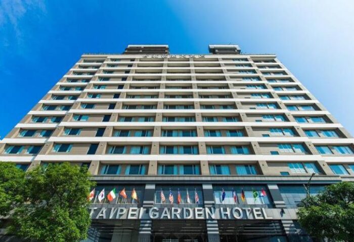 Facade of the Taipei Garden Hotel, a gay-friendly hotel in Taipei. Flags of different countries are displayed. Blue sky in the background.