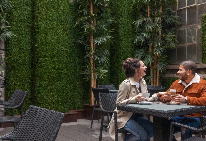 Temple Bar Inn, a gay-friendly hotel. Couple enjoying coffee at an outdoor cafe. Lush green wall and bamboo add to the ambiance. Dublin travel.