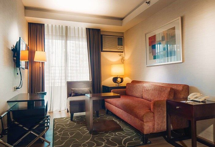 The A. Venue Hotel room. Gay-friendly hotel with a sofa, chair, TV, desk, and lamp. Comfortable lodging for gay men's travel in the Philippines.
