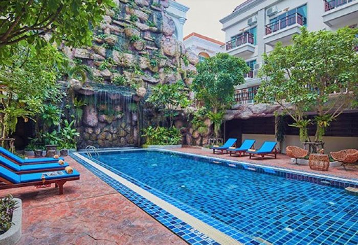 The Agate Pattaya Boutique Resort pool. Gay-friendly hotel with waterfall feature, blue lounge chairs, and tiled pool. Relaxing vacation spot.