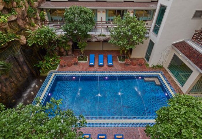 The Agate Pattaya Boutique Resort pool view. Gay-friendly hotel with waterfall feature, sun loungers, and lush greenery. Ideal for gay travelers.