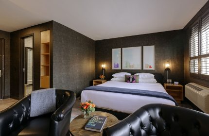 The Anndore House, part of JVD by Hyatt, gay-friendly hotel room. Bed, chairs, and table with book. Modern design, cozy feel.