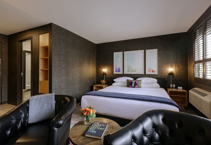 The Anndore House, part of JVD by Hyatt, gay-friendly hotel room. Bed, chairs, and table with book. Modern design, cozy feel.