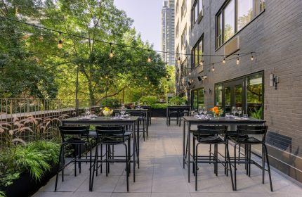 Outdoor patio at The Anndore House, part of JVD by Hyatt, a gay-friendly hotel. Tables, chairs, greenery, and string lights create a welcoming space.