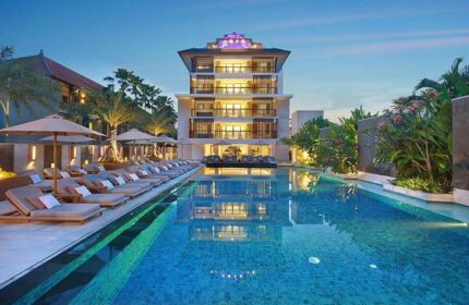 The Bandha Hotel & Suites pool at dusk. Gay-friendly hotel with lounge chairs and umbrellas. Luxury suites reflected in the water. Bali travel.