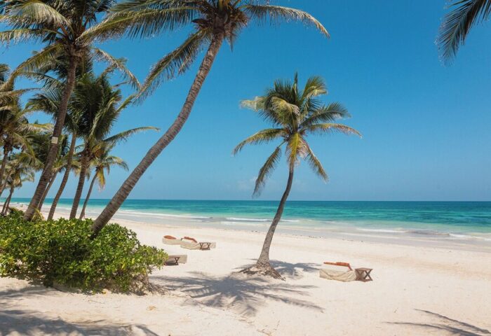 The Beach Tulum Hotel: Gay-friendly hotel with white sand, palm trees, and turquoise sea. Beach loungers invite relaxation. Tulum paradise.