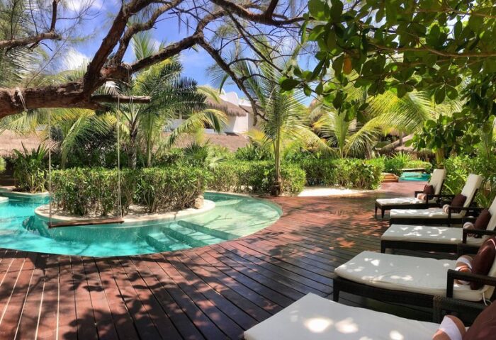 The Beach Tulum Hotel gay-friendly resort. Lush garden with pool, swing, and lounge chairs on a wooden deck. Tropical paradise, ideal for gay men.
