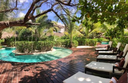 The Beach Tulum Hotel gay-friendly resort. Lush garden with pool, swing, and lounge chairs on a wooden deck. Tropical paradise, ideal for gay men.