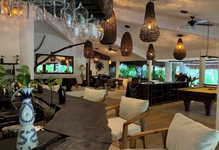 Interior of The Beach Tulum Hotel, a gay-friendly hotel. Bar, pool table, and dining area with woven light fixtures. Tropical, relaxed vibe.