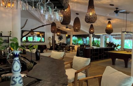 Interior of The Beach Tulum Hotel, a gay-friendly hotel. Bar, pool table, and dining area with woven light fixtures. Tropical, relaxed vibe.