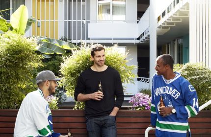 The Burrard Hotel: Three men in hockey jerseys drinking beer. Gay-friendly hotel in Vancouver with colorful doors and a social atmosphere.