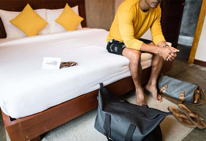 Gay traveler at The Butterfly Pea, a gay-friendly hotel. Man sits on bed in room with bags. Travel advice for gay men.