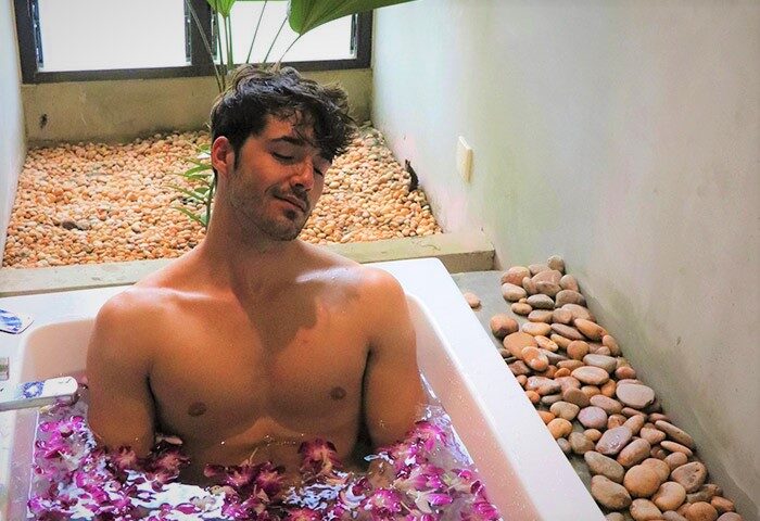 Gay-friendly hotel, The Butterfly Pea: Man relaxes in a flower-filled bathtub. A serene spa experience at this gay travel destination.