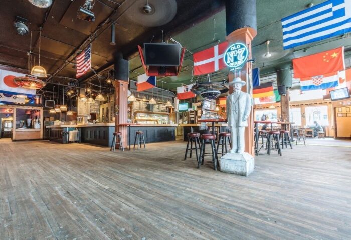 The Cambie Hostel Gastown's gay-friendly bar. Flags of the world hang above the bar area. A statue stands near bar stools.
