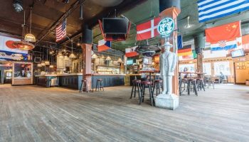 The Cambie Hostel Gastown's gay-friendly bar. Flags of the world hang above the bar area. A statue stands near bar stools.