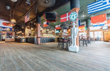 The Cambie Hostel Gastown's gay-friendly bar. Flags of the world hang above the bar area. A statue stands near bar stools.
