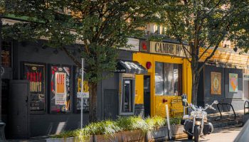 Cambie Hostel Gastown's exterior. This gay-friendly hotel features a motorcycle parked outside. A vibrant yellow facade stands out.