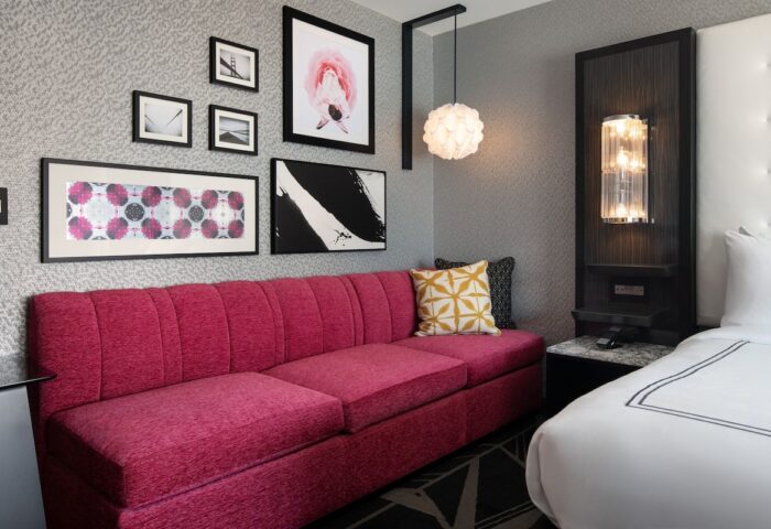 The Clancy Autograph Collection gay-friendly hotel room. A stylish pink sofa, modern art, and a cozy bed create an inviting space.