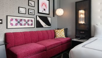 The Clancy Autograph Collection gay-friendly hotel room. A stylish pink sofa, modern art, and a cozy bed create an inviting space.