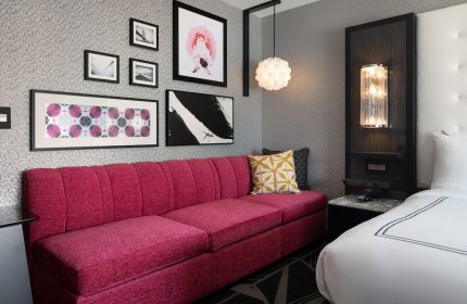 The Clancy Autograph Collection gay-friendly hotel room. A stylish pink sofa, modern art, and a cozy bed create an inviting space.