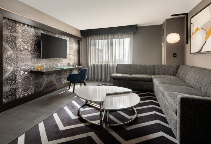 The Clancy Autograph Collection gay-friendly hotel room. Modern design with a desk, TV, sectional sofa, and stylish decor. A comfortable stay.