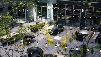 The Clancy Autograph Collection gay-friendly hotel courtyard with tables, chairs, plants, and string lights. Modern outdoor space.