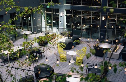The Clancy Autograph Collection gay-friendly hotel courtyard with tables, chairs, plants, and string lights. Modern outdoor space.