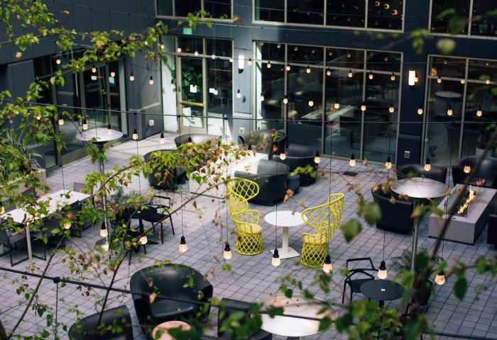 The Clancy Autograph Collection gay-friendly hotel courtyard with tables, chairs, plants, and string lights. Modern outdoor space.