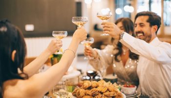 Friends toasting at The Clancy Autograph Collection, a gay-friendly hotel. Champagne glasses raised in celebration, pastries on the table.