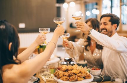 Friends toasting at The Clancy Autograph Collection, a gay-friendly hotel. Champagne glasses raised in celebration, pastries on the table.