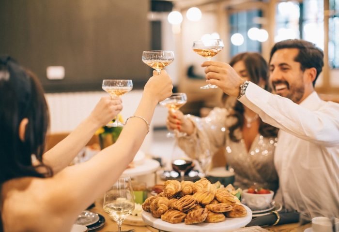 Friends toasting at The Clancy Autograph Collection, a gay-friendly hotel. Champagne glasses raised in celebration, pastries on the table.
