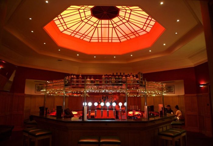 Interior of The Clarence, a gay-friendly hotel. Bar area with bottles, glasses, and an illuminated octagonal ceiling. Great spot for gay travel.