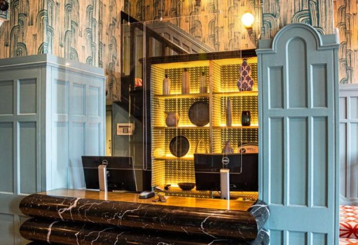The Clarence, a gay-friendly hotel. Reception area with a marble desk, blue wall decor, and illuminated display case. Upscale design.