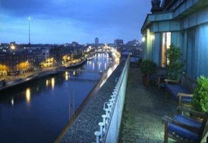 Night view from The Clarence, a gay-friendly hotel. The Liffey River flows through Dublin. Outdoor seating on a terrace. Gay travel.