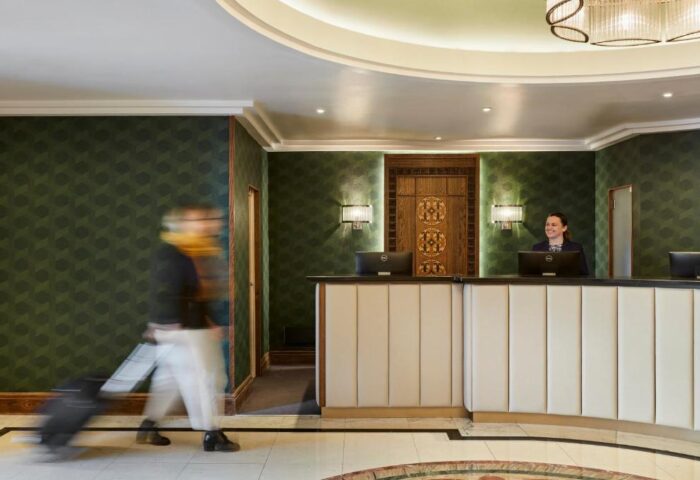 The Clermont London Charing Cross hotel lobby. Check-in desk, staff, and a guest with luggage. Gay-friendly hotel, stylish design, and welcoming atmosphere.