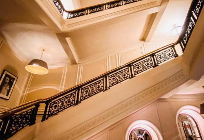 Staircase at The Clermont London Charing Cross, a gay-friendly hotel. View looking up through the center of the stairwell with ornate railings.