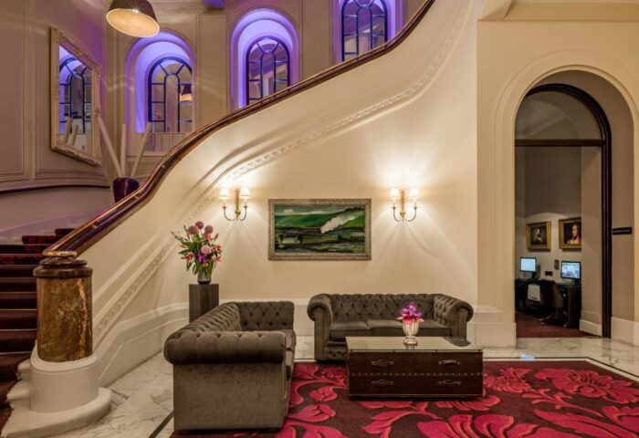 The Clermont London Charing Cross gay-friendly hotel lobby. Elegant staircase, seating area, and computer room. Luxury LGBTQ+ travel.