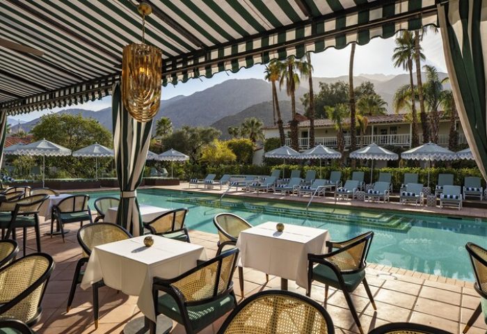 The Colony Palms Hotel pool view. Gay-friendly hotel with mountain backdrop, sun loungers, and striped umbrellas. Palm Springs resort.