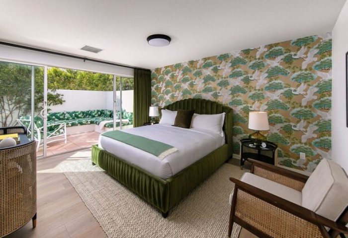 The Colony Palms Hotel, gay-friendly hotel room. Green velvet bed, patterned wallpaper, and a private patio. Luxury travel.