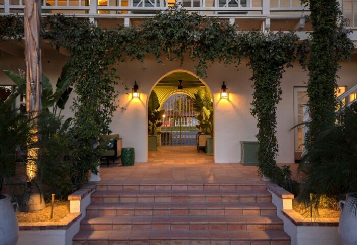 Entrance to The Colony Palms Hotel, a gay-friendly hotel. Steps lead to an arched entrance with lush greenery. Palm Springs gay travel.