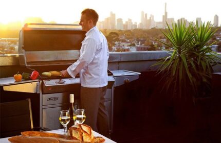 The Cullen Melbourne Art Series gay-friendly hotel: Man grilling with wine, bread, and Melbourne skyline view. Rooftop dining experience.