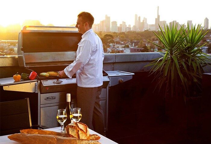 The Cullen Melbourne Art Series gay-friendly hotel: Man grilling with wine, bread, and Melbourne skyline view. Rooftop dining experience.