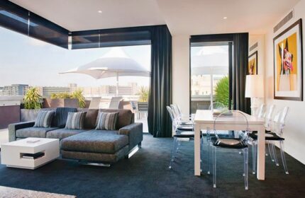 The Cullen Melbourne Art Series gay-friendly hotel room. Modern interior with a lounge area, dining table, and balcony with city views.