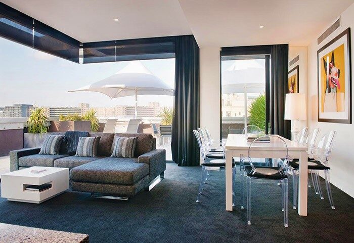 The Cullen Melbourne Art Series gay-friendly hotel room. Modern interior with a lounge area, dining table, and balcony with city views.