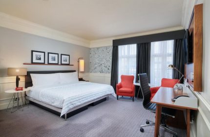 The Dilly, gay-friendly hotel room. Bedroom with a king-size bed, desk, and two red armchairs. Modern decor. Ideal for gay travel.