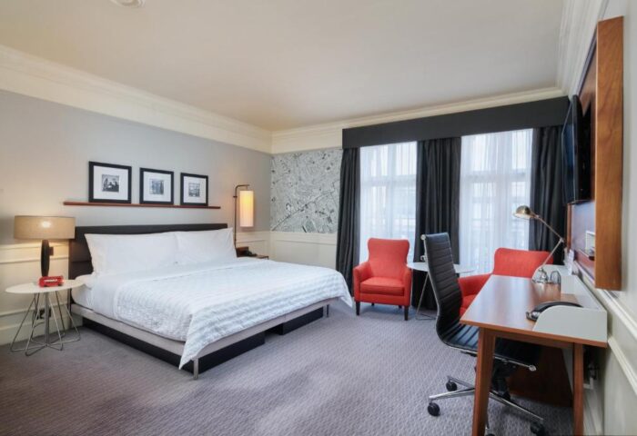 The Dilly, gay-friendly hotel room. Bedroom with a king-size bed, desk, and two red armchairs. Modern decor. Ideal for gay travel.